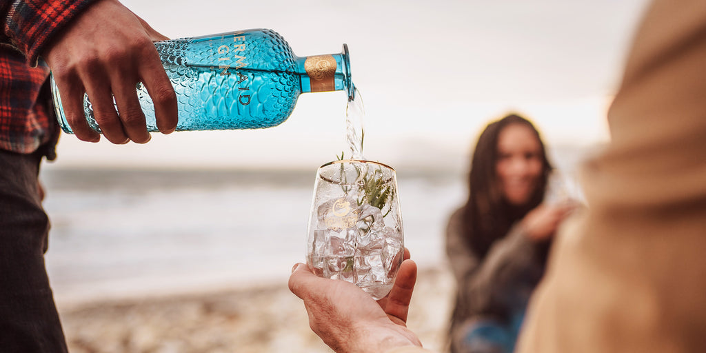 Mermaid gin being poured into a tumbler glass at a beach campfire gathering