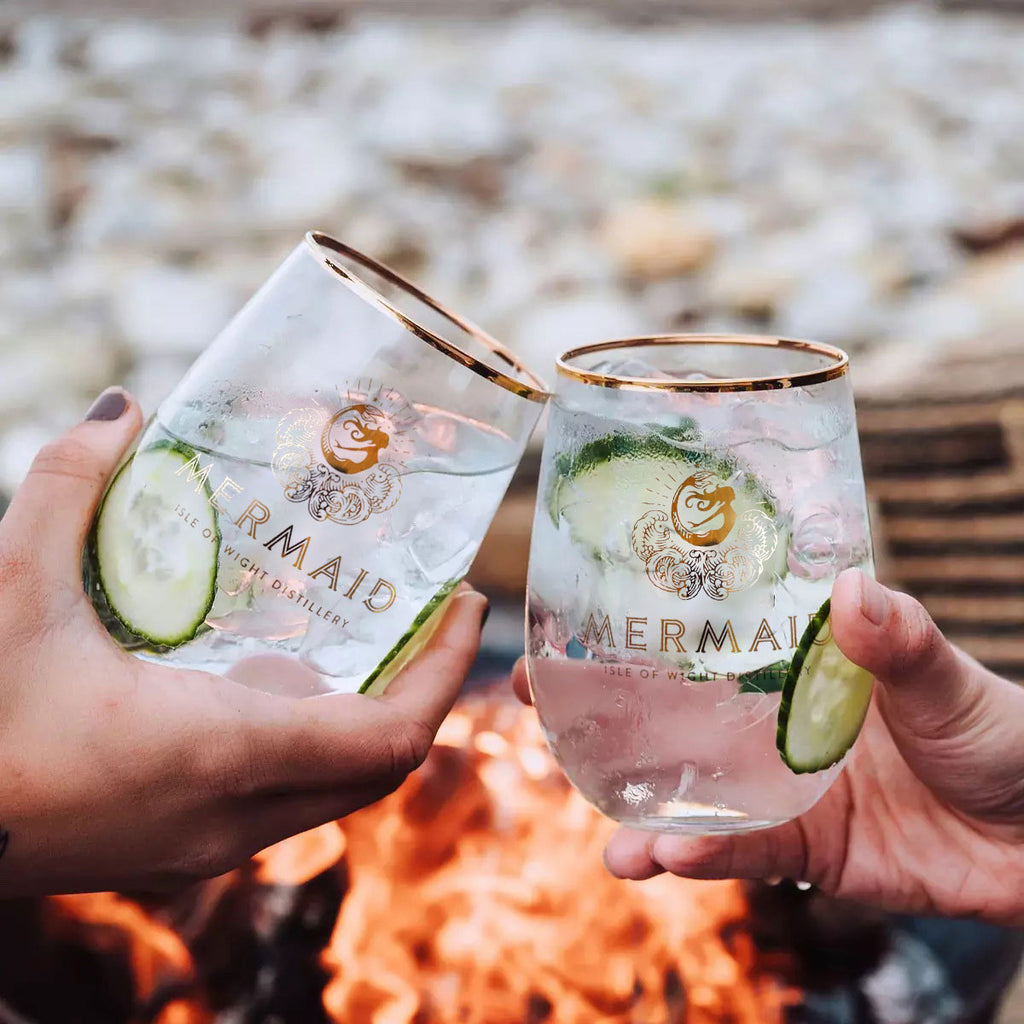Cheers! Two Mermaid Gin tumbler glasses in front of fire.